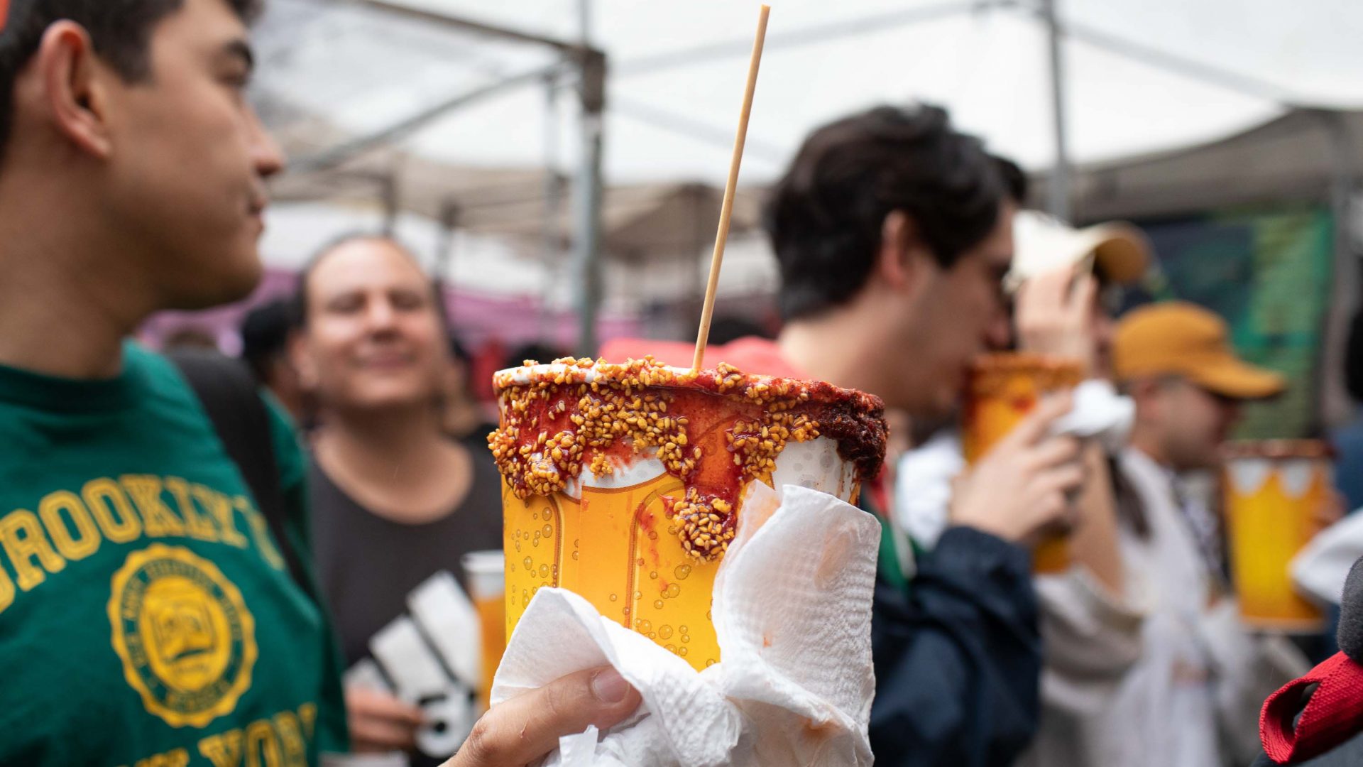 A person holds a michelada cup in a crowd of people.