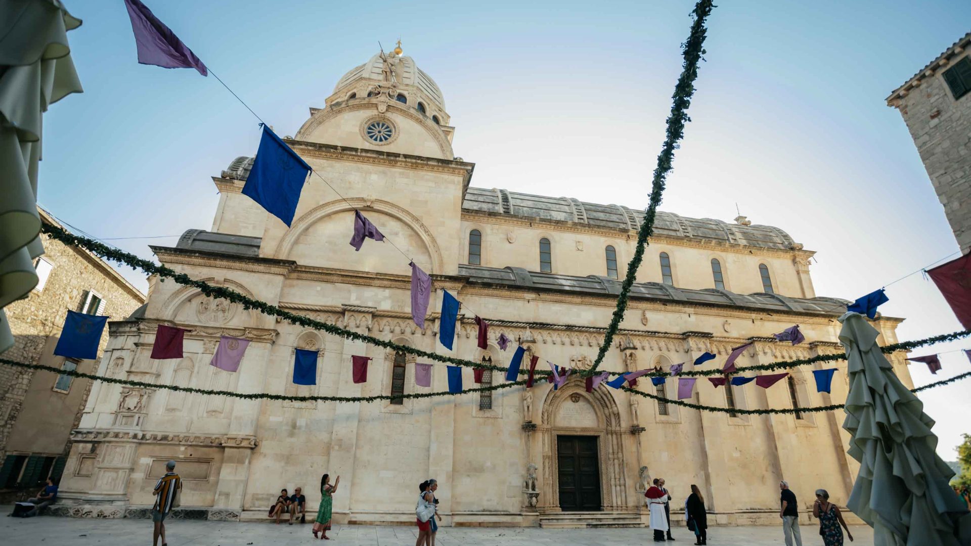 A church with people in front of it and bunting flying in the sky.