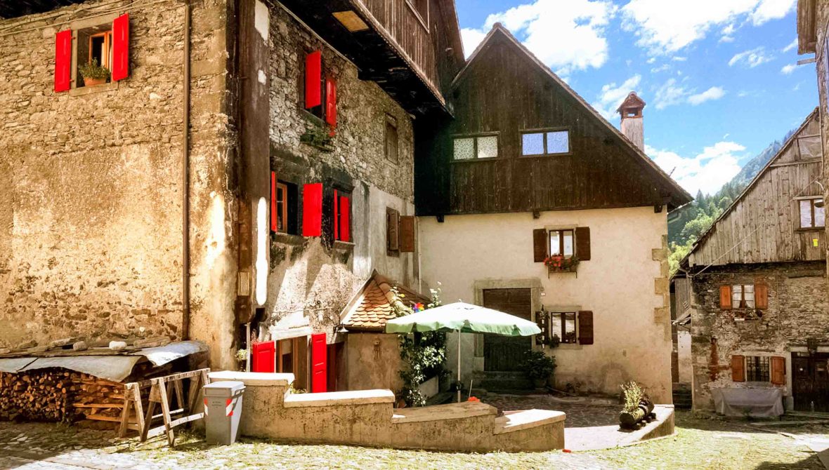 The village of Pesaris. There is a stone building with a wood pile alongside it and an umbrella over a table.